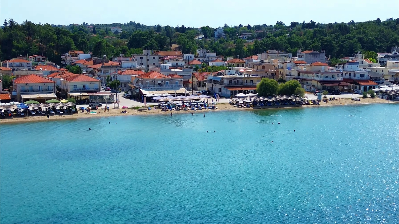 Plaža blizu Soluna sa tirkiznim morem, ležaljkama i kućama uz obalu